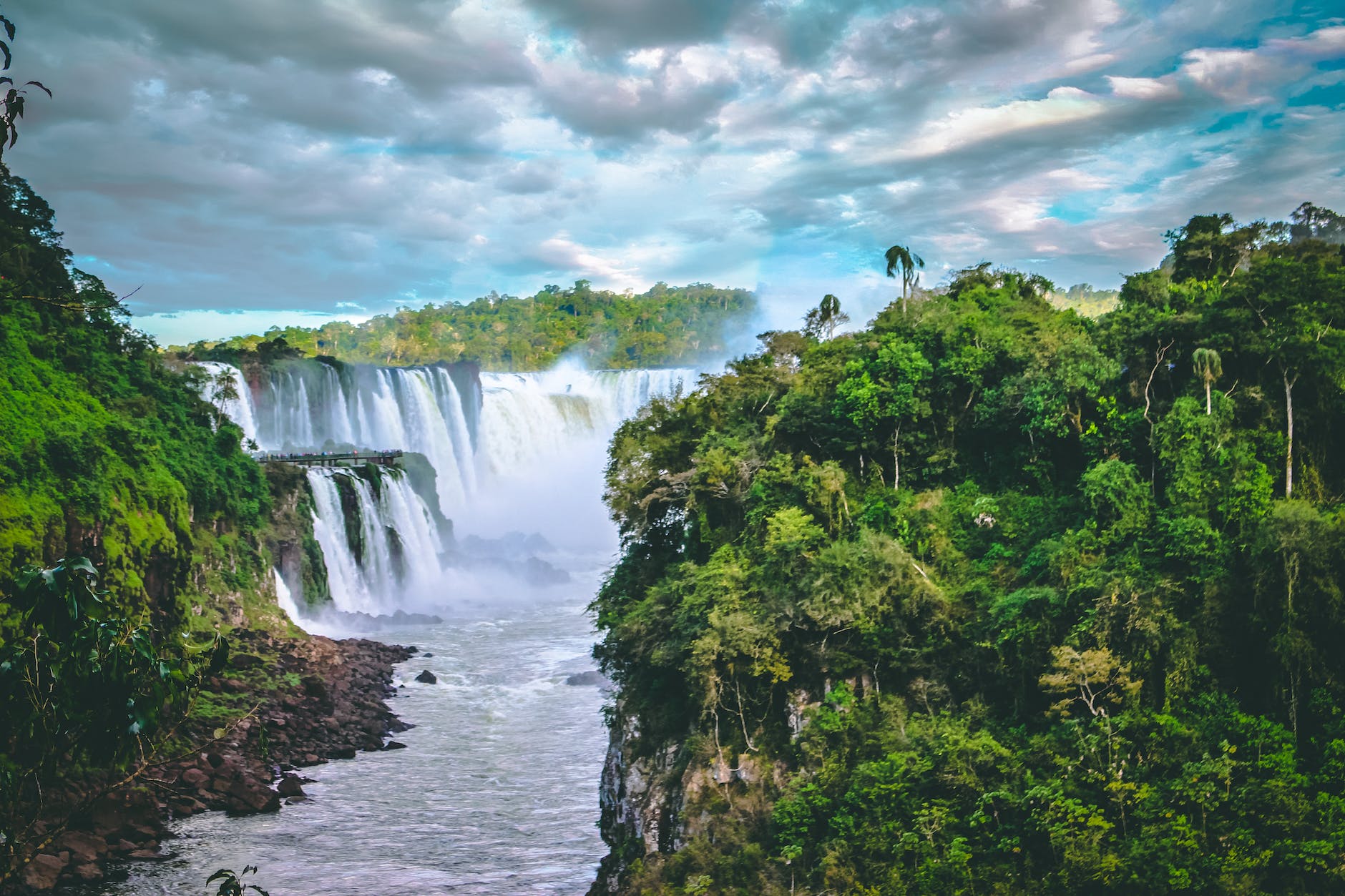 scenic photo of waterfalls between trees under cloudy sky